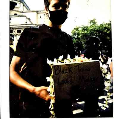 A person wearing a mask holds a sign advocating for Black Trans Lives Matter at a London protest.