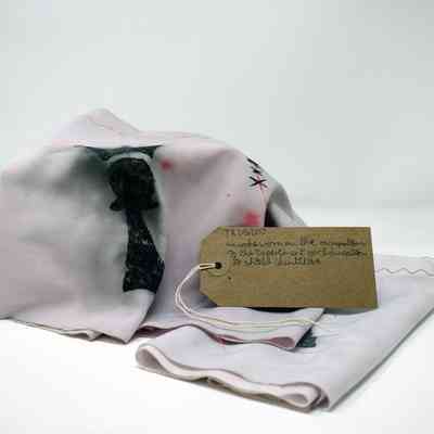 Two pale pink snoods decorated with the Trans Kids Deserve Better 'Pawn with a crown' logo. With a brown, handwritten luggage tag.