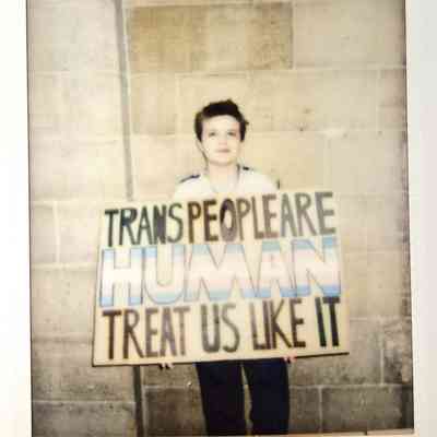 A person holds a sign that reads "Trans People Are Human, Treat Us Like It."
