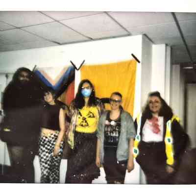 Five people pose together in front of colorful flags on a wall, smiling cheerfully indoors.