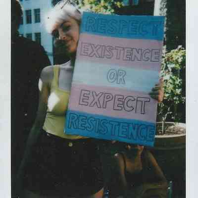A person holds a sign with the message, “Respect existence or expect resistance” outdoors.