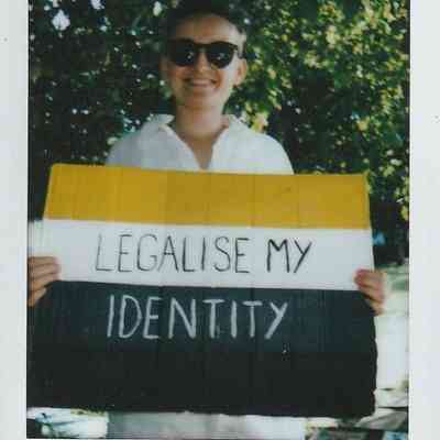 A person holding a sign with "LEGALISE MY IDENTITY" stands outdoors, wearing sunglasses.