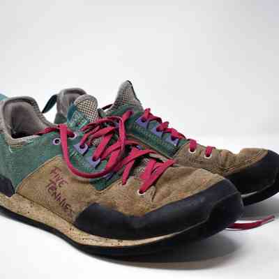 A pair of Five Ten climbing shoes. The uppers are green and brown suede and they have red laces.