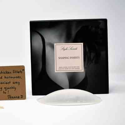 Front of a black box reading "Style Secrets Shaping Inserts. Hides under your favourite bra for even more lift and shaping" lying next to one silicone breast inserts and a brown tag with writing on it.