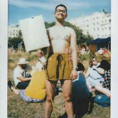 A person is holding a blank sign and standing confidently in a sunny outdoor gathering.