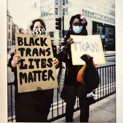 Two individuals hold signs advocating for Black trans lives during a protest on a city street.