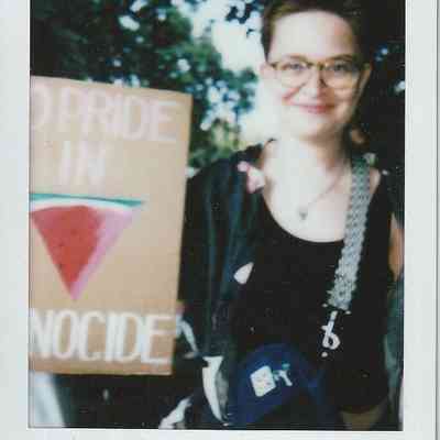 A person with glasses smiles while holding a sign with a message.