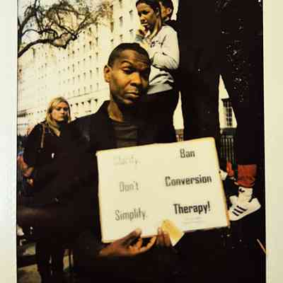 A person holds a sign that reads "Ban Conversion Therapy!" during a protest event.