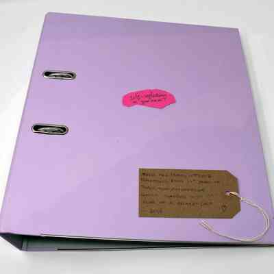 A pink folder which has a pink postit on top of it and a brown luggage tag with writing on it.
