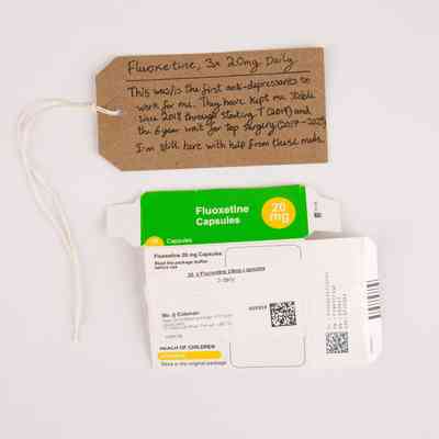 An green and white empty box for Fluoxetine 20mg. With a brown, handwritten luggage tag.