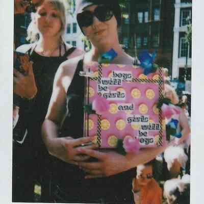 A person holding a colorful sign which says "boys will be girls and girls will be boys".