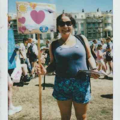 A smiling person holds a sign with hearts during an outdoor event on a sunny day.
