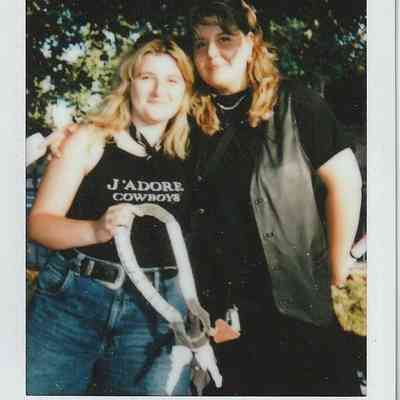 Two people smile together outdoors; one wears a "J'adore Cowboys" shirt, the other a leather vest.