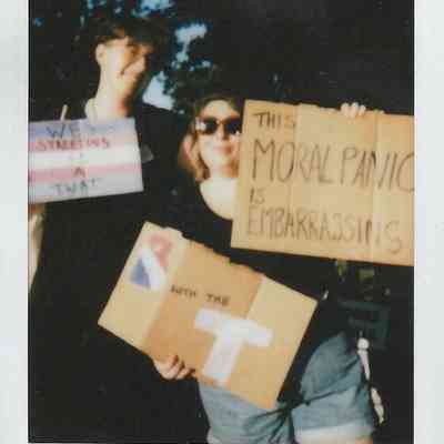 Two people hold signs expressing opinions on a controversial topic, standing outdoors with trees in the background.