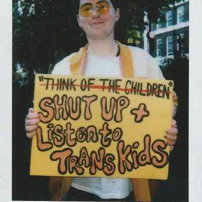 A person holds a sign reading "Shut Up & Listen to Trans Kids" at London Trans Pride.