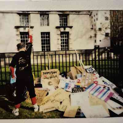 A person stands with a raised fist near a pile of protest signs outside a building.