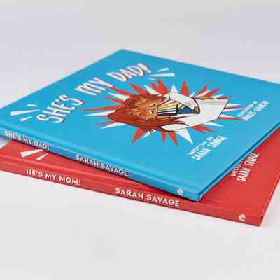 Two Children's Books - 'She's My Dad!' and 'He's My Mom!' which are blue and red and stacked on top of each other.
