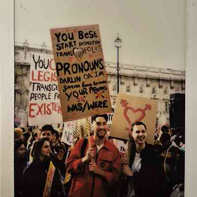 A group of people holding protest signs, one says "YOU BEST START RESPECTING TRANS FOLKS PRONOUNS DARLIN OR I'M GONNA HAVE TO MAKE YOUR PRONOUNS WAS/WERE".