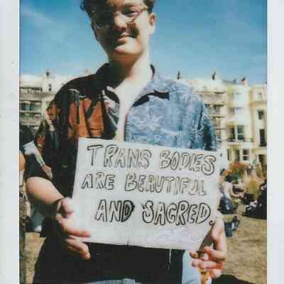 A person is holding a sign that reads, "Trans bodies are beautiful and sacred".