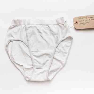Pair of white tucking pants lying on a wooden surface. The cotton string of the tag is wrapped around the gusset.