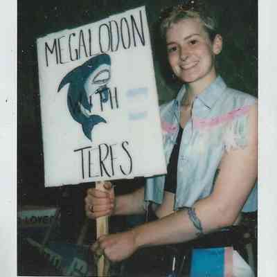 A person holds a sign reading "Megalodon With TERFS," featuring a drawing of a shark.