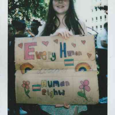 A person wearing a cap holds a colorful sign which says "Every Human Deserves Human Rights".