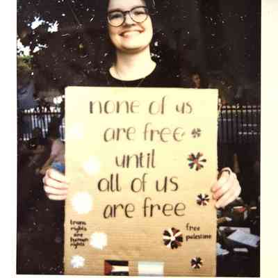 A person is smiling while holding a cardboard sign advocating freedom and equality for everyone.
