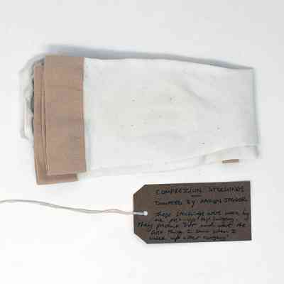 A pair of folded, beige compression stockings. With a brown, handwritten luggage tag.