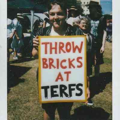 A person holds a protest sign which says "THROW BRICKS AT TERFS".