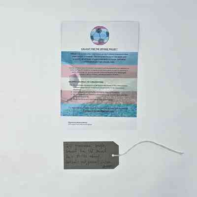 A flyer calling for trans masc people to take part in The Offside Project and give their experiences of football. The background is in the trans pride colours. With a brown, handwritten luggage tag.
