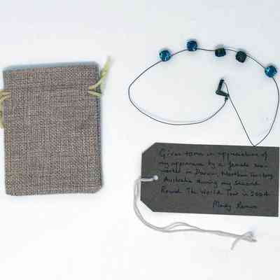 A necklace strung with 5, blue, glass, beads, a small hessian drawstring back and a brown, hand written luggage tag.