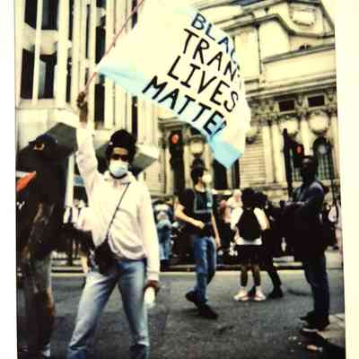 A person in a mask holds a sign that reads, "Black Trans Lives Matter" at a protest.