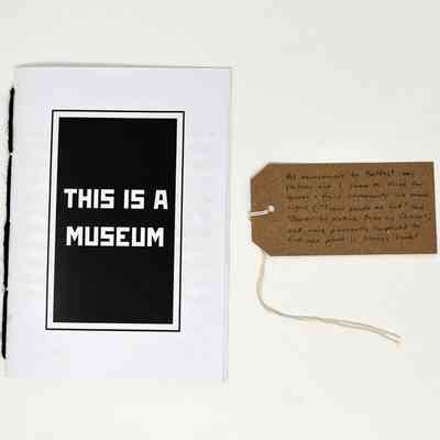 The image shows a booklet titled "THIS IS A MUSEUM" next to a handwritten tag.