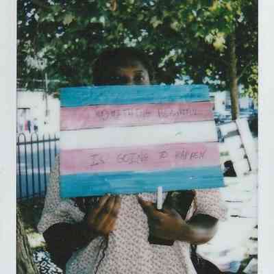 A person holds a sign with a hopeful message, standing outside near trees on a sunny day.