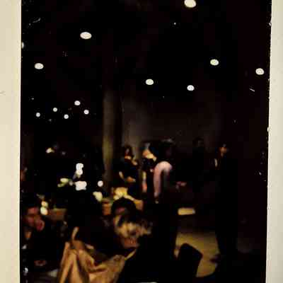 A dark lit polaroid which vaguely a room with lots of people and tables.