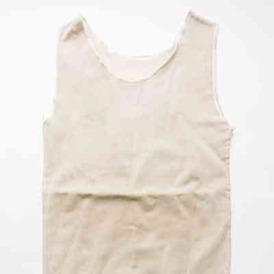 A white chest binder is laid flat on a white surface, showing its front with a light brown stain on the bottom edge.