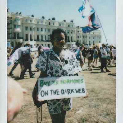 A person stands in a crowd holding a sign which says "Buy Yr Hormones On The Dark Web".