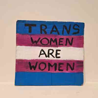 A placard with trans pride colors displays "Trans Women Are Women" in bold letters.