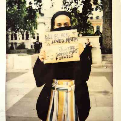 A person holds a sign reading "All Black Lives Matter" and "Juntos Somos Más Fuertes".