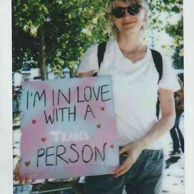 A person in sunglasses holds a sign reading "I’m in love with a trans person,".