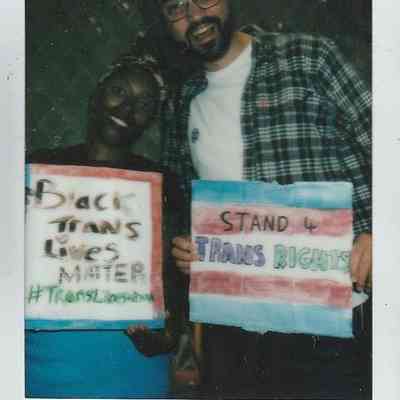 Two individuals hold signs supporting trans rights with smiles at an event marked TP Brighton '24.