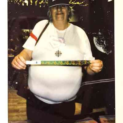 A person wearing a hat and glasses holds a decorated stick in a room with lights.