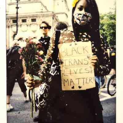 A person holds flowers and a sign reading "Black Trans Lives Matter" at a demonstration.