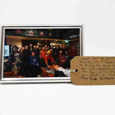 The image shows a group photo from a Trans Pride assembly with a handwritten tag detailing the event.