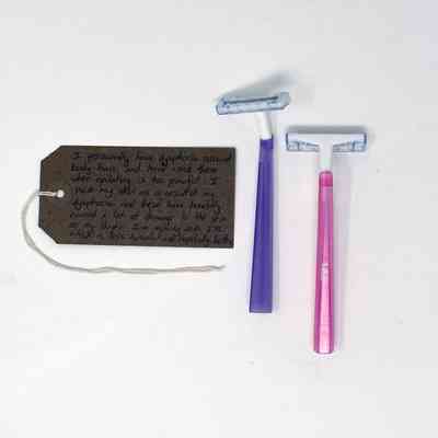 2x razors with pink and purple handles, white plastic heads and metal blade, clear plastic blade shield.