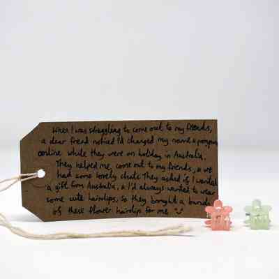 Two small flower hair clips (one orange, one green) with a brown handwritten luggage tag.