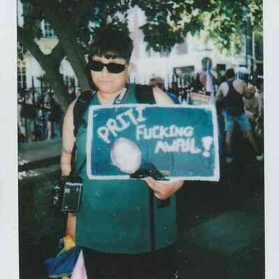A person in sunglasses holds a sign which says "Priti Fucking Awful".