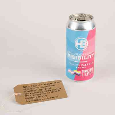 An empty can of "Transgender Day of Visibility" Pale Ale, brewed by Horsforth Brewery. The can is pink and blue and features the trans and non-binary flags. Also, a brown, handwritten luggage tag.