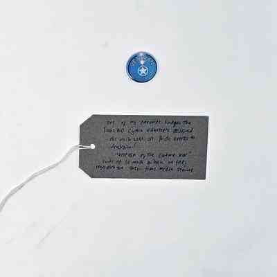 Blue pin badge inscribed "VETERAN OF THE CULTURE WAR" around a white 5 pointed star in a circle. With a brown handwritten luggage tag.