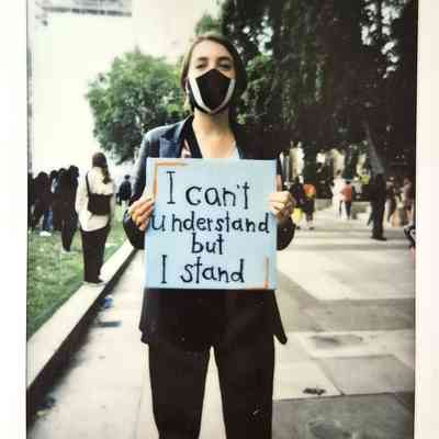 A person wearing a mask holds a sign reading "I can't understand but I stand" during a protest.